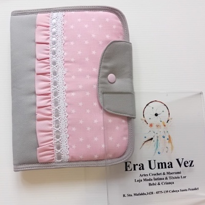 Carteira rosa com estrelas brancas, renda e fecho cinzento, junto a placa transparente com texto e apanhador de sonhos
