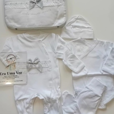 Conjunto de roupa de bebé branco com acessórios e saco decorado.