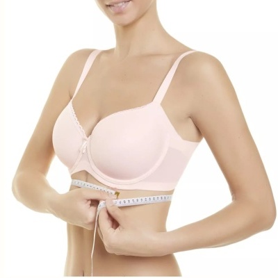 Mulher a medir a circunferência sob o peito com fita métrica enquanto usa soutien rosa claro