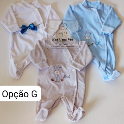 Três macacões de bebé em tecidos branco, azul claro e bege, cada um com bordado ou laço e botões frontais.