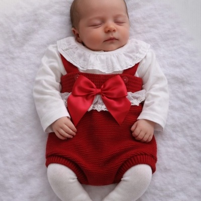 Bebé com roupa vermelha e branca deitada em superfície branca