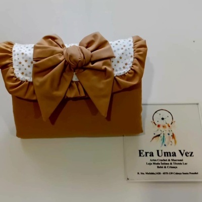 Mala castanha acolchoada com laço e detalhes de estrelas sobre superfície branca