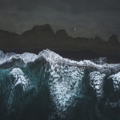 Costa com ondas brancas e praia de areia preta vista de cima