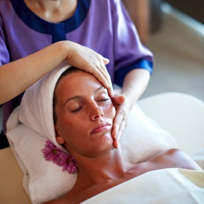 Mulher a receber massagem facial com toalha branca e flor roxa no spa