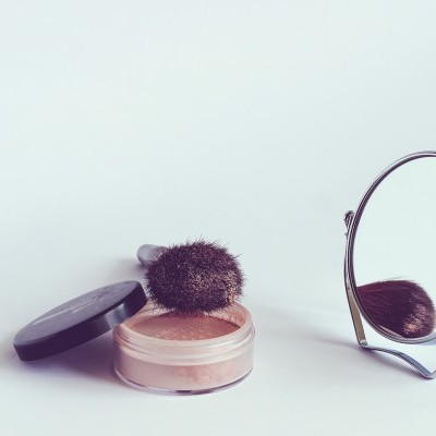 Pó facial solto com pincel e espelho redondo sobre superfície branca
