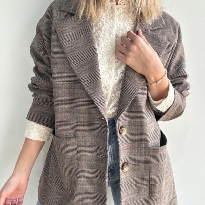 Blazer xadrez castanho com botões e bolsos, sobre blusa branca de renda e jeans azuis.