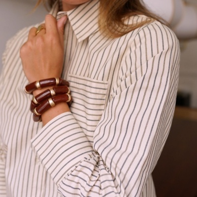 Camisa branca às riscas finas pretas com pulseiras castanhas e douradas no pulso