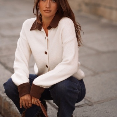 Mulher com camisola branca e castanha, jeans azul e mala castanha agachada na rua