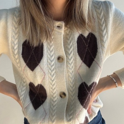 Cardigan de malha bege com corações castanhos escuros e botões castanhos.