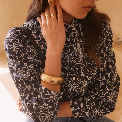 Blusa feminina azul escura com padrão floral branco e acessórios dourados.