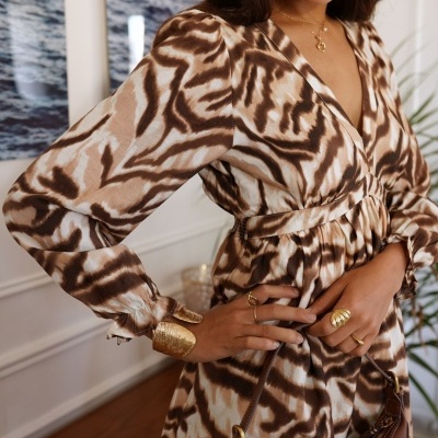 Vestido comprido com padrão animal castanho e bege, mangas compridas, acessórios dourados e mala castanha.