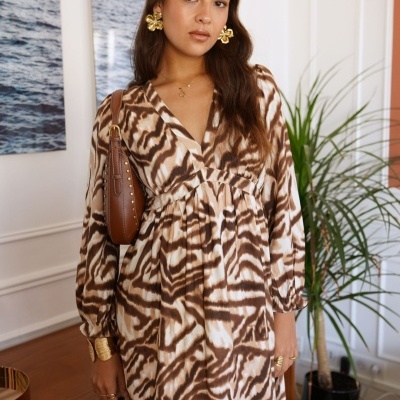 Vestido animal print castanho e branco com acessórios dourados em ambiente interior