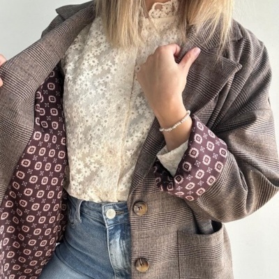 Casaco xadrez castanho aberto mostrando forro estampado, blusa branca de renda e calças de ganga