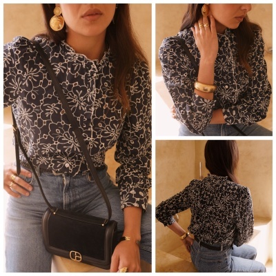 Blusa feminina azul escuro com flores brancas, gola com babado e mangas compridas, usada com calças de ganga azuis e acessórios dourados