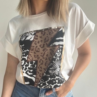 T-shirt branca com estampado de raio castanho com padrão de pele animal e fundo de manchas preto e branco, usada com calças de ganga azuis.