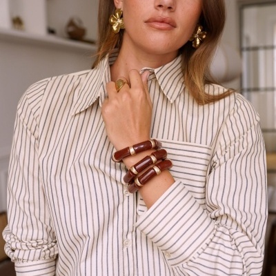 Mulher com camisa às riscas brancas e pretas, pulseiras de madeira castanha e brincos dourados grandes