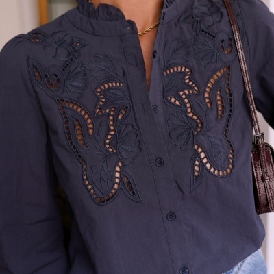 Blusa preta bordada com recortes e botões, calças de ganga e mala castanha.