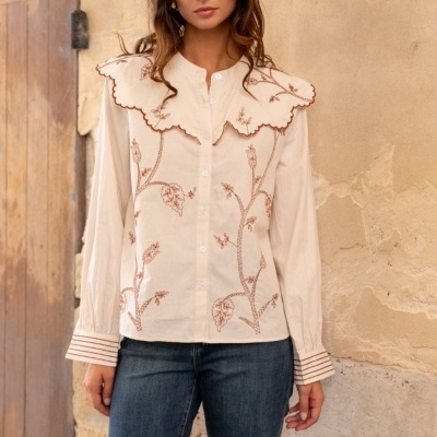 Camisa bege claro com bordados florais castanhos e gola oversized, com jeans escuros