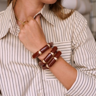 Mulher com camisa de riscas brancas e azuis, pulseiras de madeira castanha e brinco dourado em forma de flor.