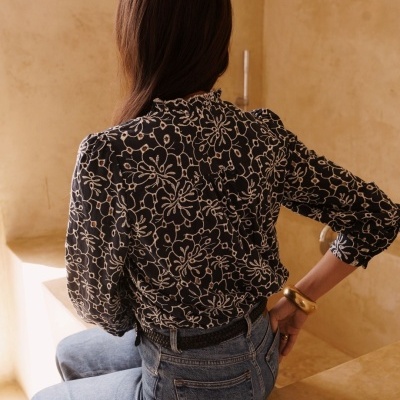 Blusa preta com padrão floral branco usada por trás com jeans azuis claros