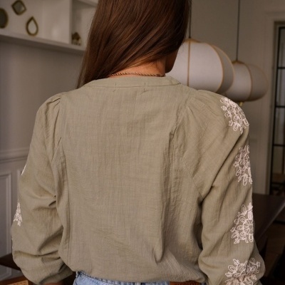 Blusa feminina verde-oliva com bordados brancos e calças de ganga azul claro vista de costas