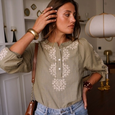 Blusa verde-oliva bordada com calças de ganga em ambiente interior moderno