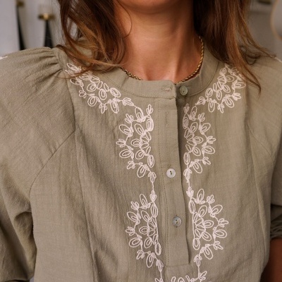 Blusa verde-oliva com bordado branco floral ao redor da gola e botões frontais, usada por mulher