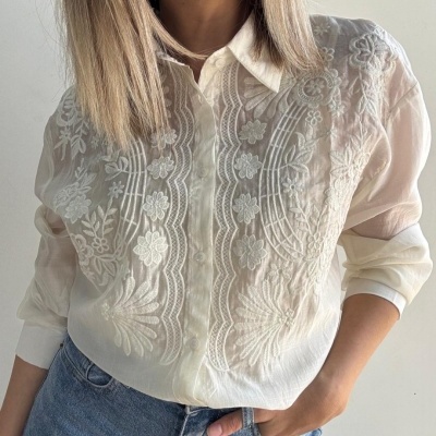 Camisa branca bordada de mulher com mangas compridas e calças de ganga azuis