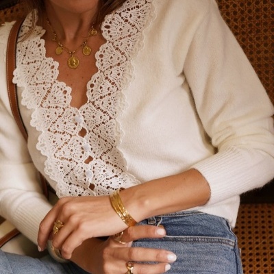 Mulher usando suéter branco com gola em renda e calças de ganga azuis sentada em cadeira de vime