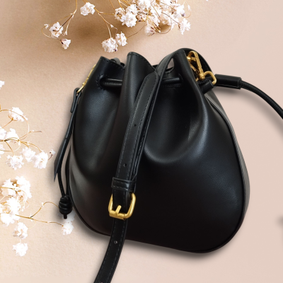 Mala preta em couro com alça e fivela dourada em fundo bege com flores brancas