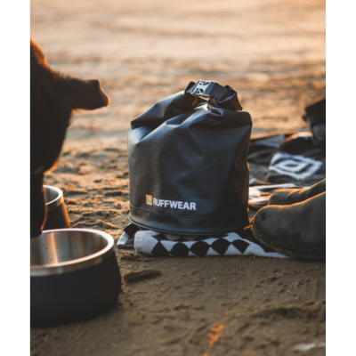 Saco de viagem preto RUFFWEAR com fecho, perto de tigelas e botas na areia