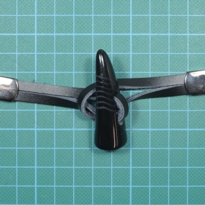 Suporte para máscara facial preto com extremidades prateadas sobre superfície quadriculada verde