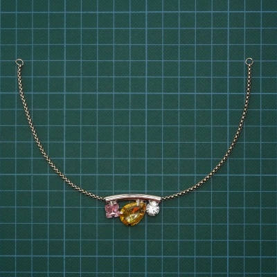 Colar dourado com pedras coloridas sobre fundo verde cuadriculado