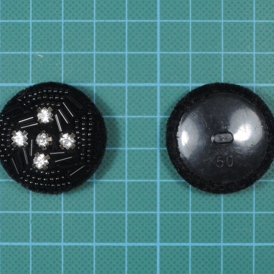 Dois botões pretos redondos, um com cristais e outro com inscrição 150 60, sobre fundo quadriculado verde.