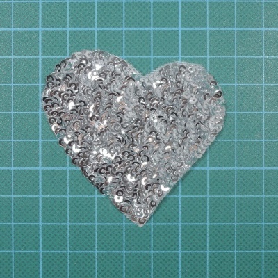 Almofada em forma de coração com lantejoulas prateadas sobre fundo quadriculado verde