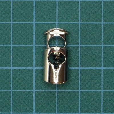 Dispositivo metálico prateado com mola sobre superfície quadriculada