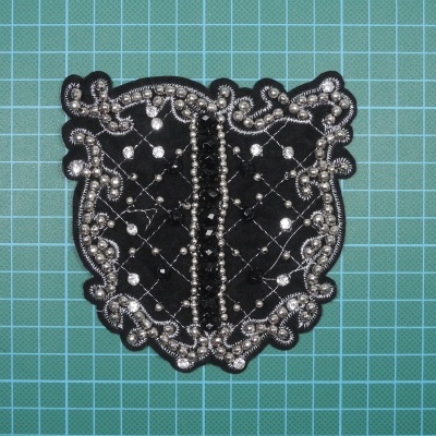 Apliqué preto com bordado prateado e pedras brilhantes, sobre fundo verde quadriculado