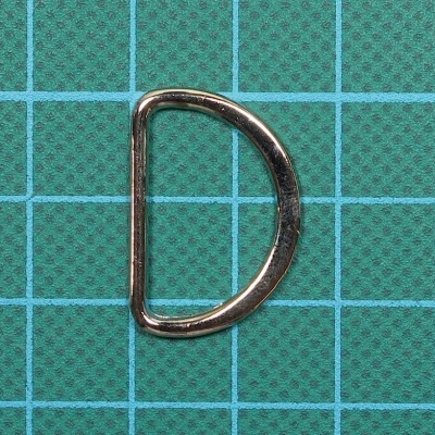 Argola metálica em formato de D sobre fundo verde quadriculado