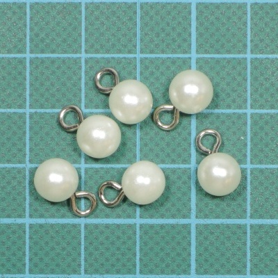 Pendentes redondos que simulam pérolas com argolas metálicas prateadas sobre superfície verde quadriculada