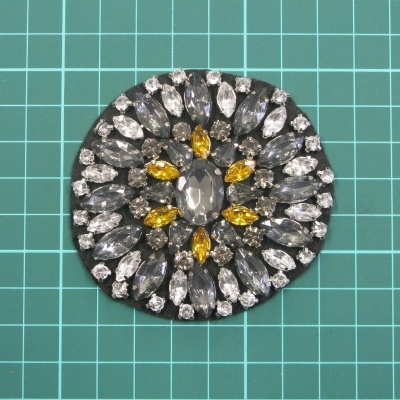 Broche redondo com pedras cinza, amarelas e transparentes em padrão circular