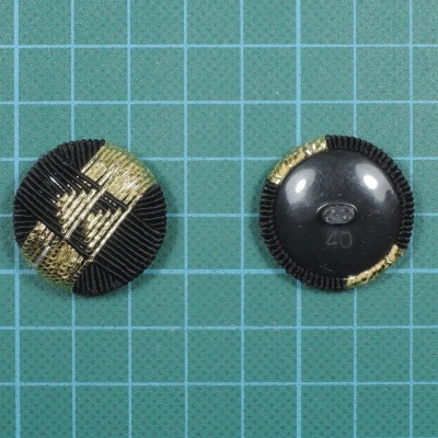 Dois botões redondos pretos e dourados em fundo quadriculado verde