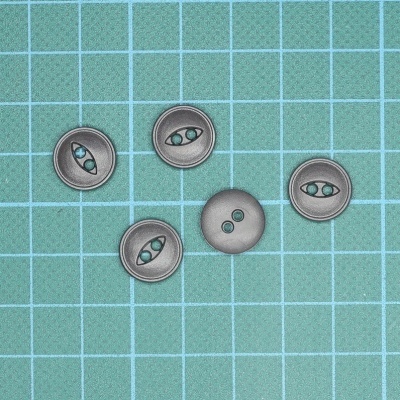 Cinco botões cinza com padrão verde dispostos sobre superfície quadriculada verde