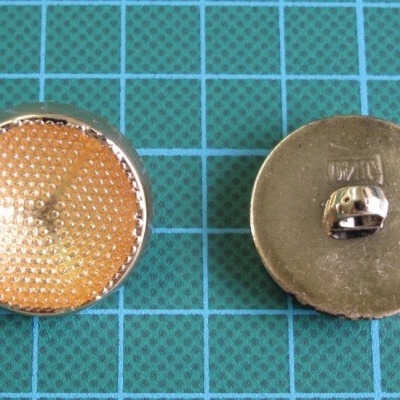 Dois botões metálicos redondos com frente amarelada texturizada sobre superfície quadriculada