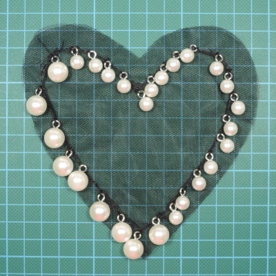 Colar ou pulseira de pérolas em forma de coração sobre superfície quadriculada azul-esverdeada.