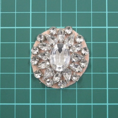 Broche redondo com pedras acrílicas transparentes num fundo verde quadriculado