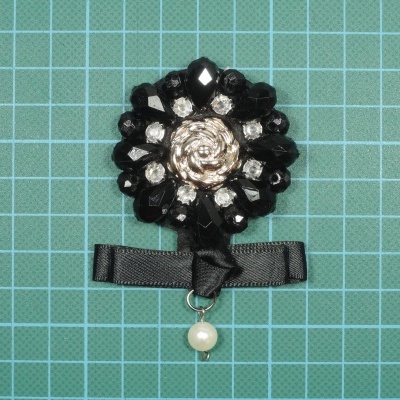 Broche floral com pedras pretas, strass, centro dourado, fita preta e pérola