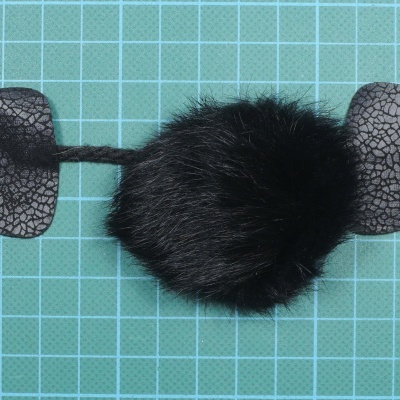 Pompom preto com detalhes laterais de tecido sintético sobre superfície verde quadriculada