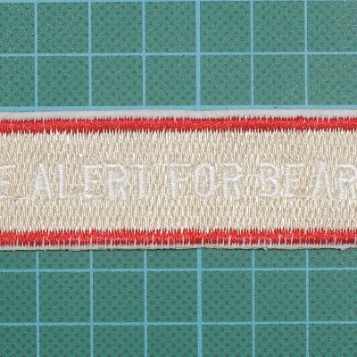 Aplicação bordada retangular com texto em branco e borda vermelha