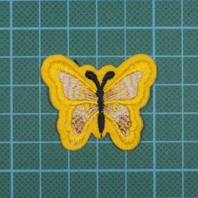 Patch bordado amarelo em forma de borboleta sobre fundo verde com linhas de grade