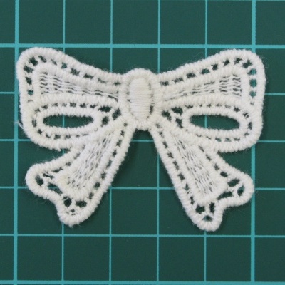 Laço decorativo de renda branca sobre fundo verde quadriculado.